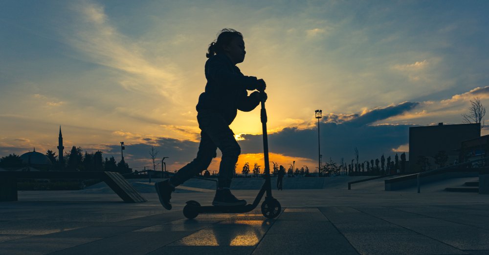 En pappa och ett barn i åttaårsåldern gör en high five i en lummig svensk skatepark, där barnet står nöjt bredvid sitt rullande åkdon